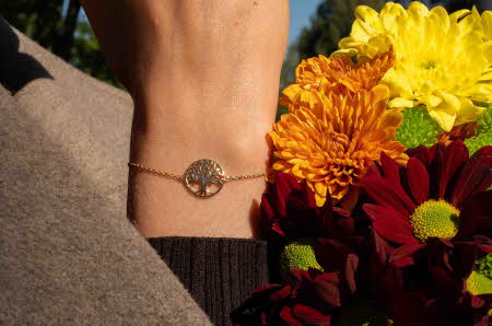 En hånd med et armbånd med livets tre ved siden av blomster i høstfarger.