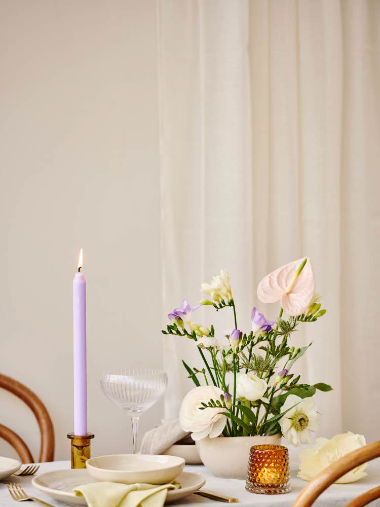 Bord med duk, lysestake, glass, lys og blomster Blå vegg, lysestake og bilde på veggen