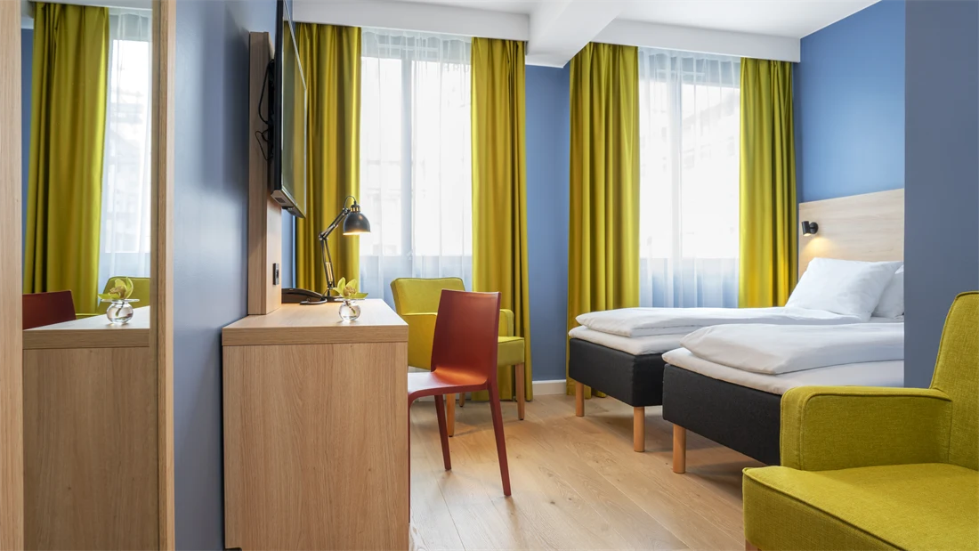 Gul stol, separate senger, blå vegger, gule gardiner og skrivebord på standard rom twin på Thon Hotel Astoria