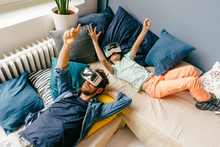 Fugleperspektiv på mann og jente som ligger i senga med VR-briller. Foto til artikkel om gaver til pappatyper på farsdag.