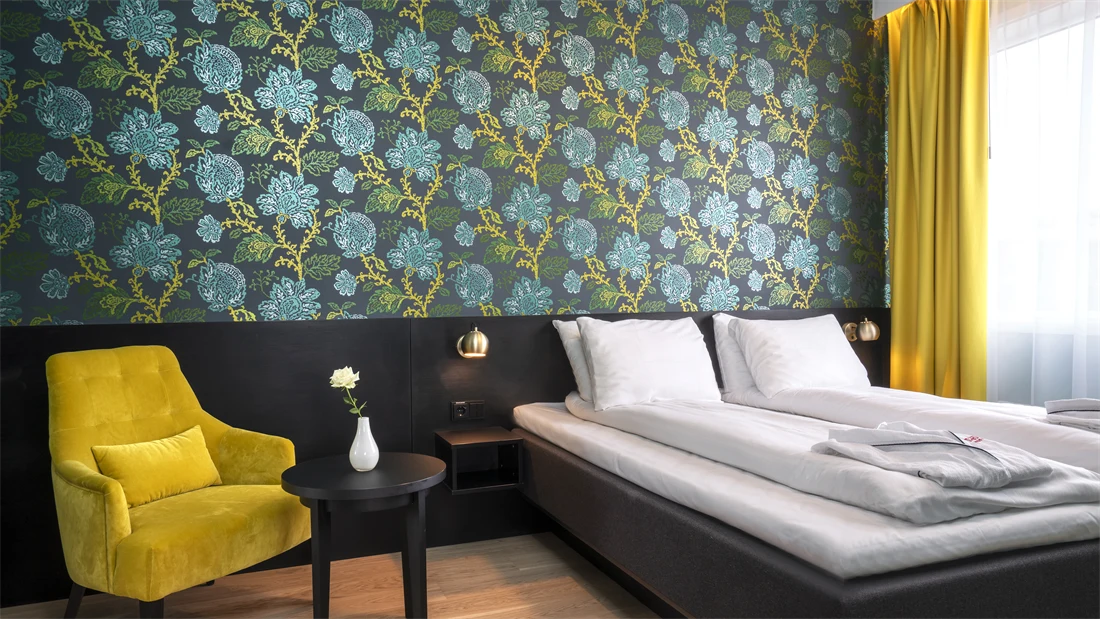 Grønn og turkis mønstrete tapet med blomster, gul stol med rundt bord og dobbeltseng i suite på Thon Hotel Kirkenes