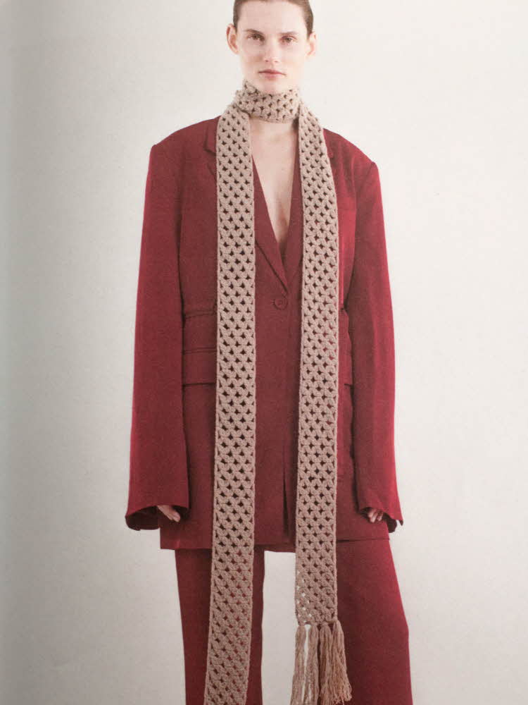Modell med burgunder dress og langt, tynt og beige strikket skjerf.