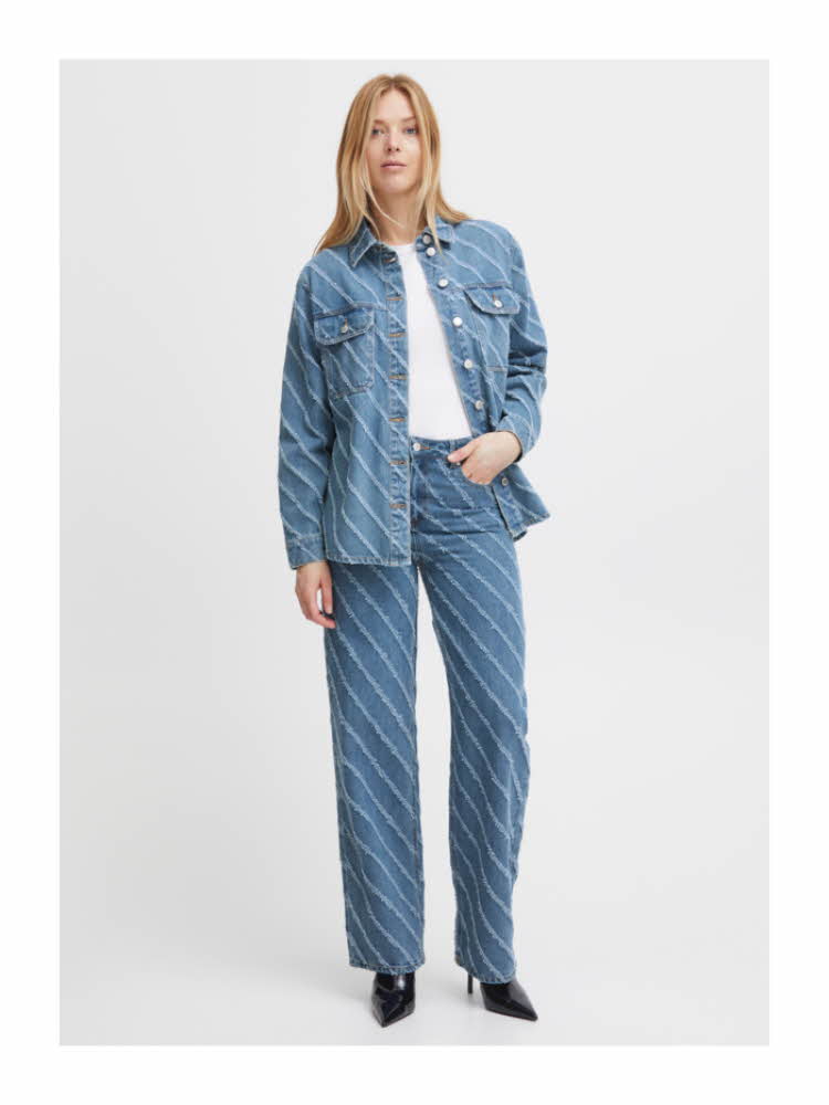 Damemodell med lyst langt hår som har på seg denimskjorte, hvit topp, jeans og sorte støvletter