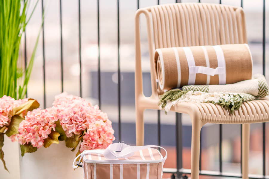 En beige stol med et piknikteppe står ved siden av en kjølebag og blomster på en balkong