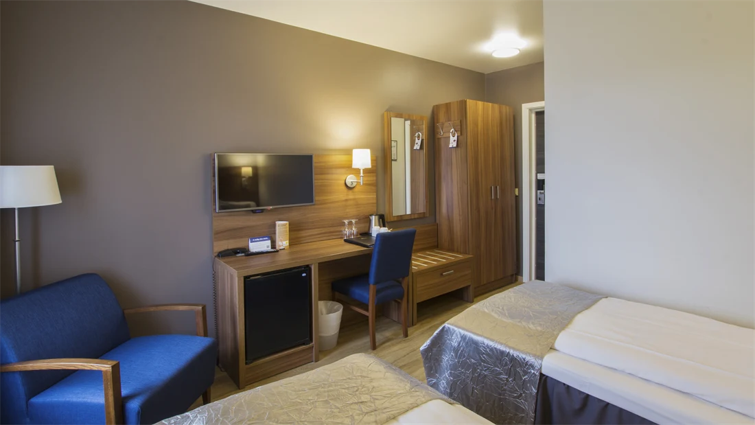 Skrivebord, TV, blå stol og seng i twin rom på Thon Hotel Horten