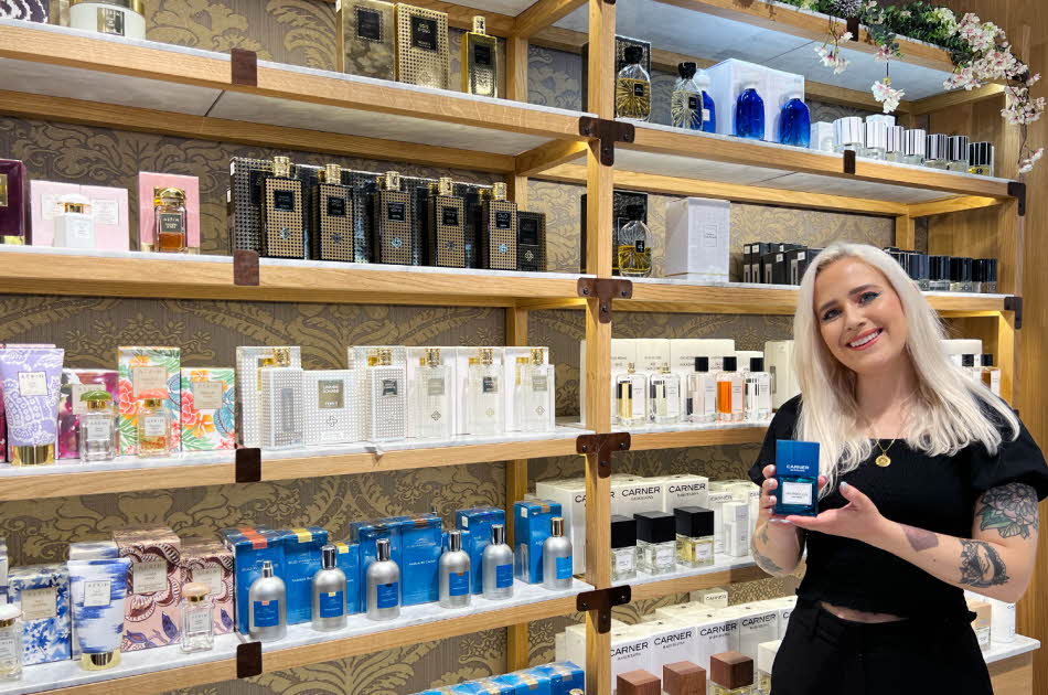 Kvinnelig butikkansatt på Fredrik & Louisa holder en parfyme foran en hylle med produkter