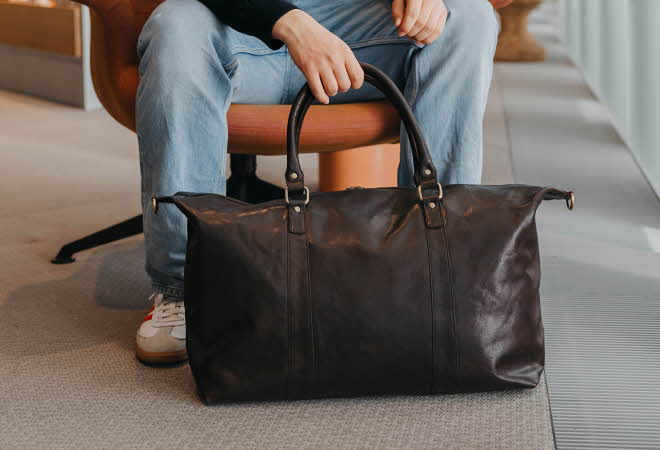 En person som sitter i en stol og holder på en brun bag som står på gulvet