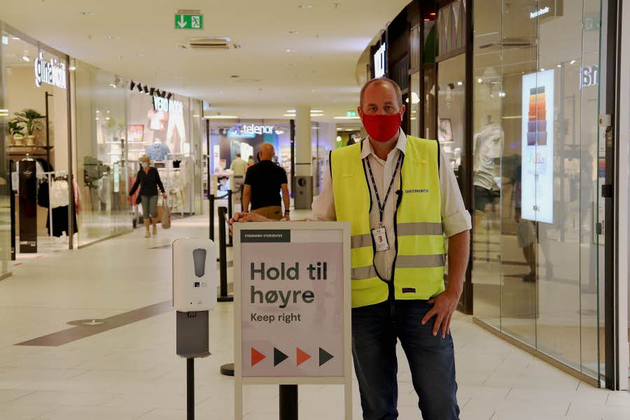 Bilde av mann med munnbind ved plakat i kjøpesenter
