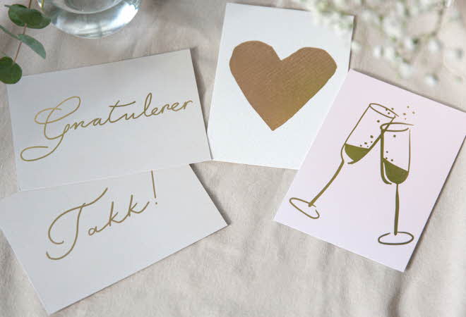 Tre gratulasjonskort på lys stoff, med ordet "Gratulerer", et gullhjerte, og to champagneglass.