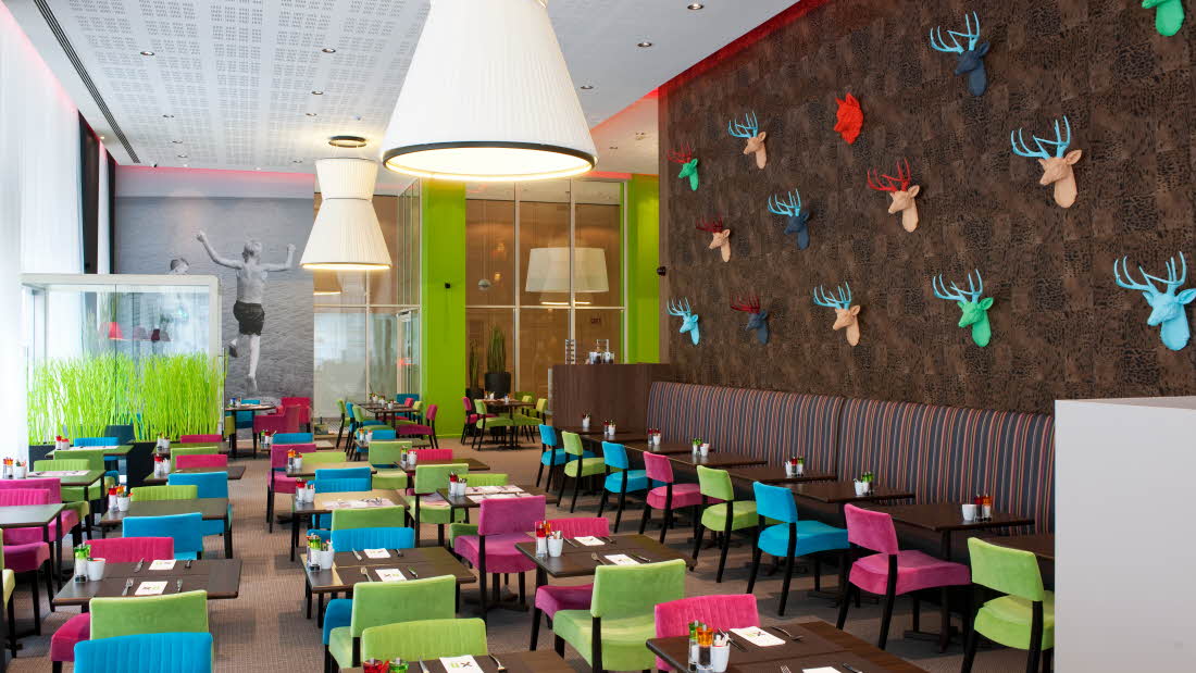 Frokostsalen med fargerike stoler. På veggen henger hjortehoder i plast, i forskjellige farger.