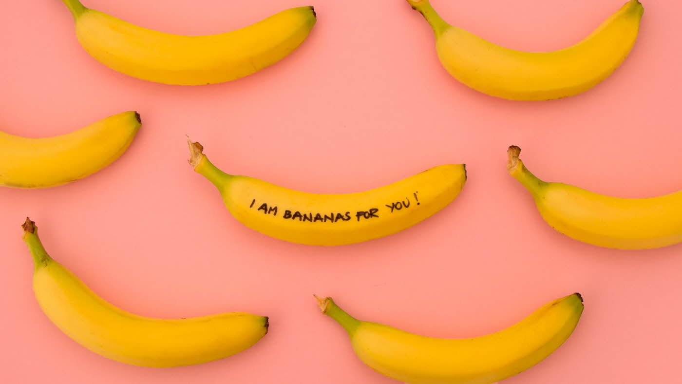 Syv gule bananer på rosa bakgrunn, på den midterste bananen står det "I am bananas for you!"