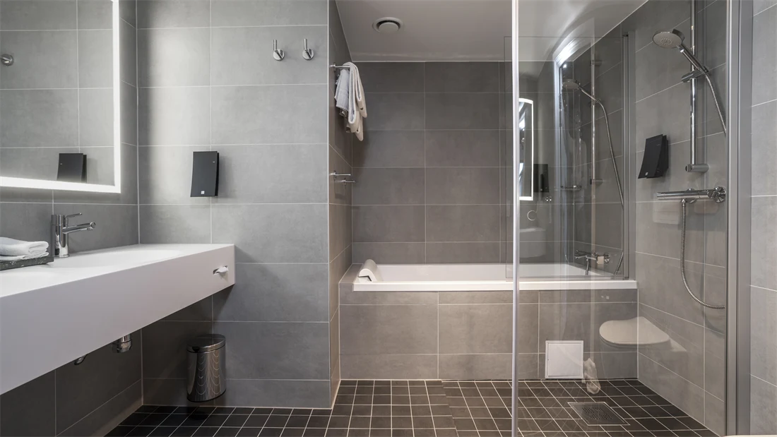 Badekar, grå gulvfliser, grå veggfliser, dusj, vask, speil, toalett
