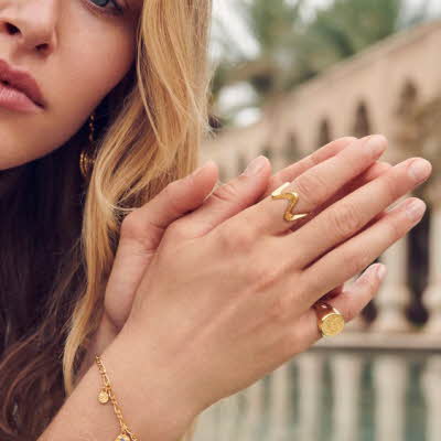 Dame holder hendene foran seg med ringer og armbånd i gull