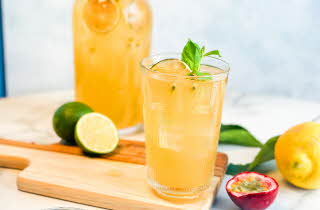 et glass med lemonade, dekorert med frukt rundt på bordet og en glassflaske med lemonade i bakgrunnen
