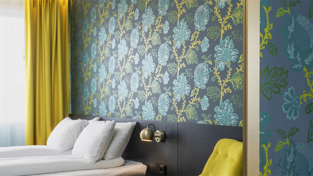 Blå og grønn mønstrete tapet med blomster, gul stol og rundt bord, dobbelsteng og gule gardiner i dobbeltrom på Thon Hotel Kirkenes.
