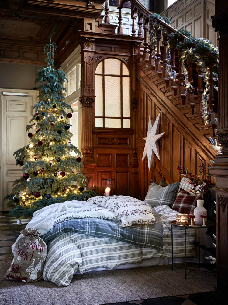 Seng med deilig sengetøy i stort herskapshus foran juletre dekket julebord og julestjerne