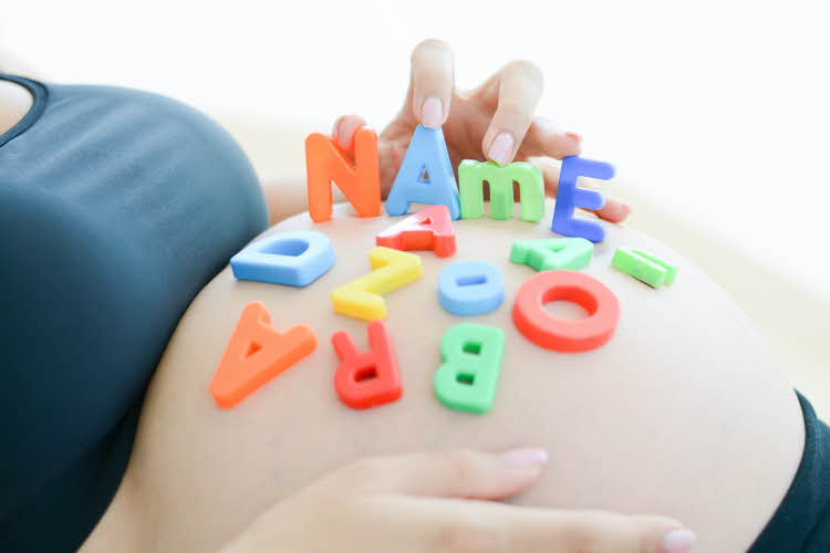 gravid kvinne med leke bokstaver som staver ut name på magen