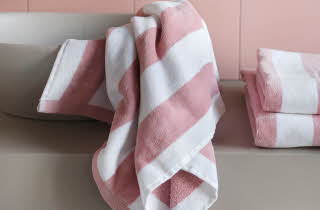 En vask med et rosa og hvitt håndkle i, og en bunke med de samme rosa og hvite håndklærne ved sien av