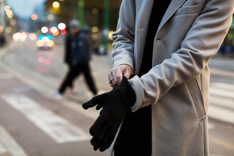 Nærbilde av mann med lys beige frakk som tar på hansker