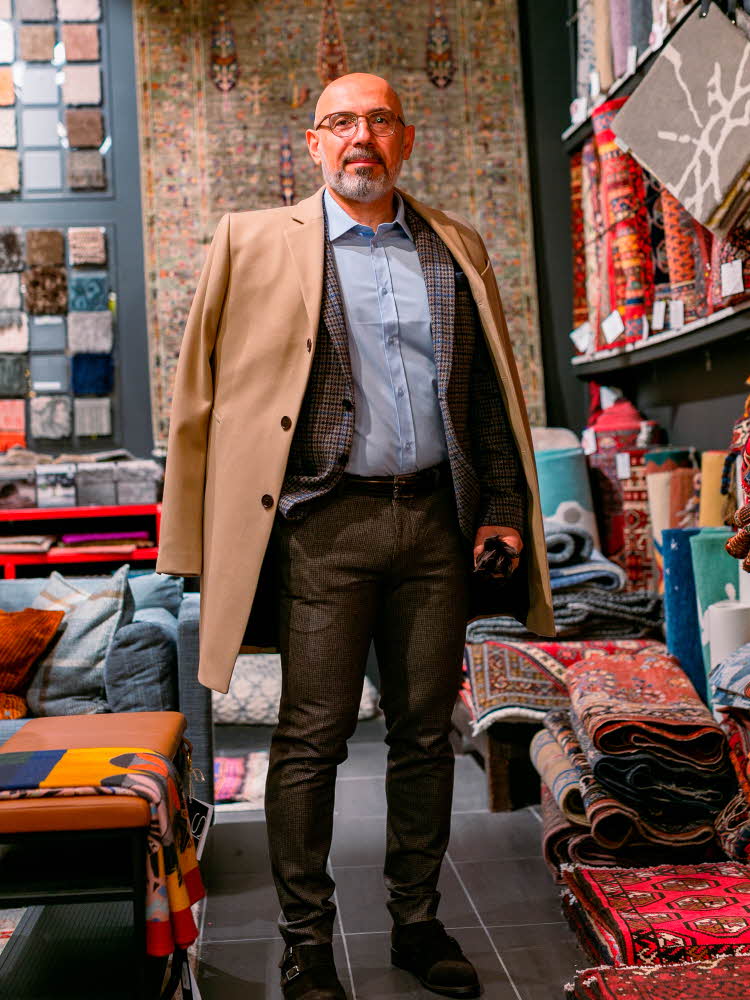 mann i brungrå dressbukse, lyseblå skjorte, mønstret dressjakke og beige kåpe