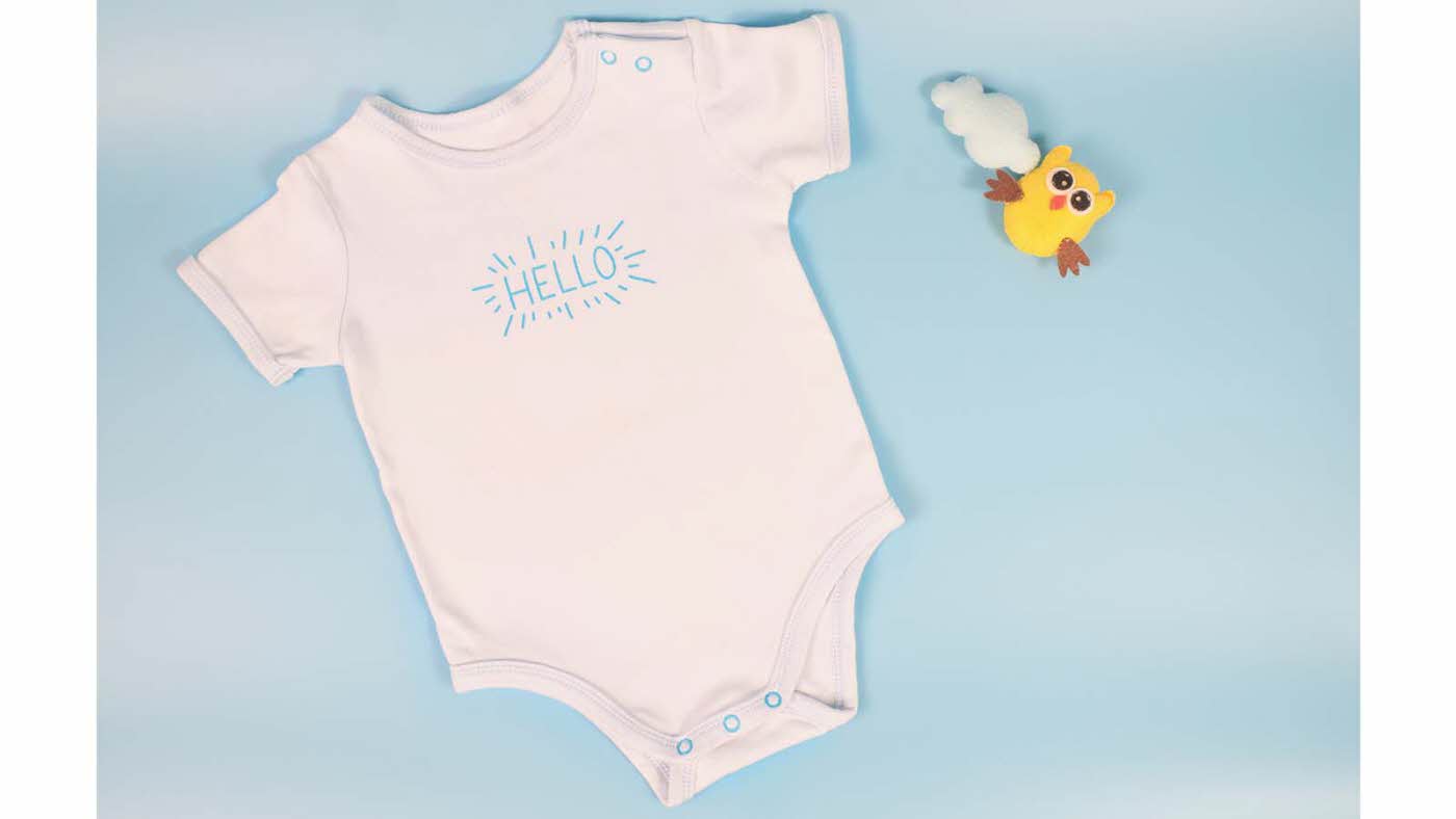 En hvit body til nyfødt som det står "Hello" på. Liten, gul leke ved siden av. Lyseblå bakgrunn. Illustrasjonsfoto til artikkel om kaker til babyshower.
