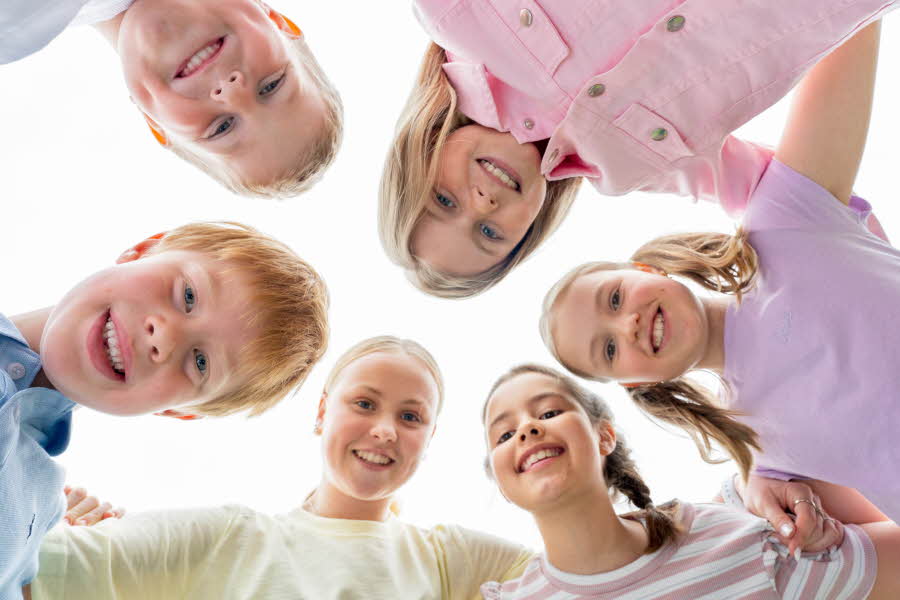 6 smilende barn holder står i runding og titter ned på kameraet