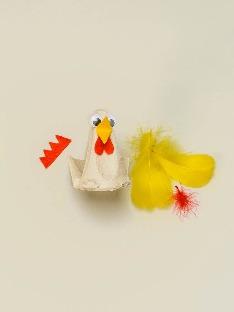 En eggekartong omgjort til en høne med øyne og nebb, resten av utstyret ligger ved siden av  En eggekartong omgjort til en høne som mangler vinger og hanekam