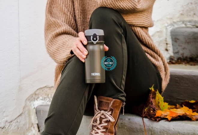 En person som sitter på en trapp ute med en termoskopp i hånden.