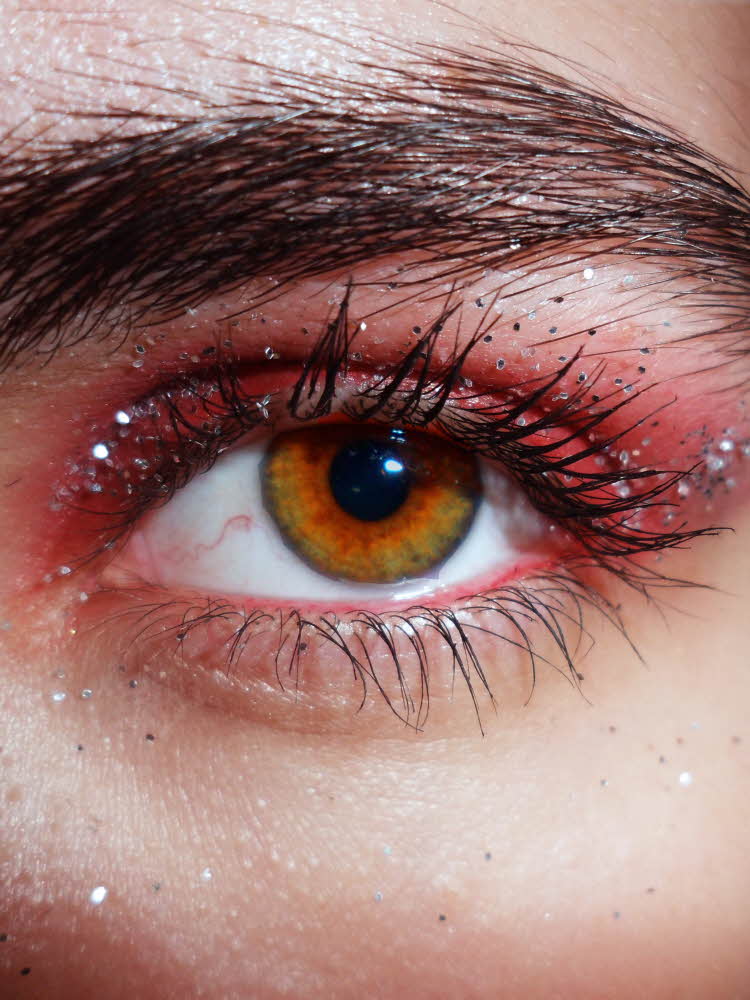 Nærbilde av øye sminket med rød øyenskygge og sølvglitter