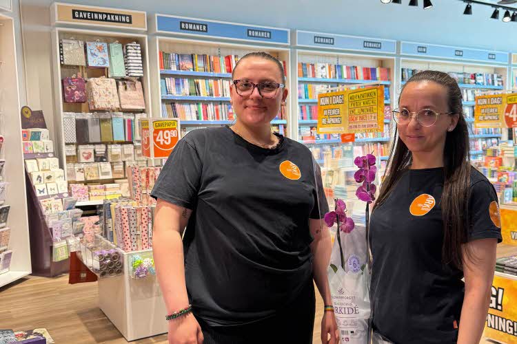 To ansatte i ARK står og smiler til kameraet i butikken