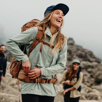 Dame som smiler med friluftsklær med to andre på et fjell