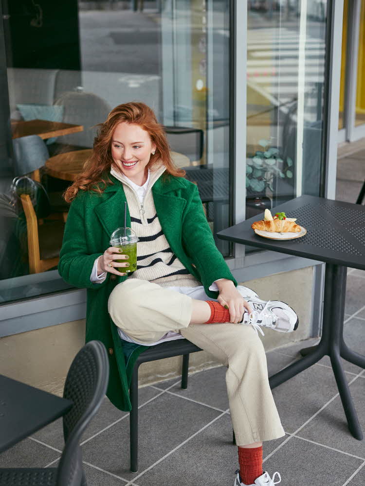 Dame med grønn jakke Dame som sitter på en kafe