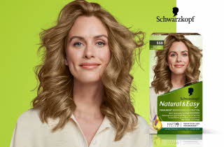 Reklamebilde for Schwarzkopf Natural & Easy permanent hårfarge, viser en kvinne med glansfullt, bølgete blondt hår ved siden av produktesken med samme bilde og grønn bakgrunn.