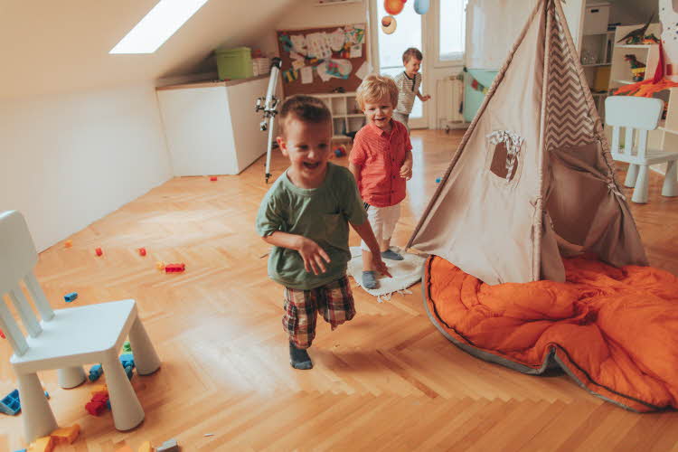 Tre gutter løper og ler på barnerom ved leke-tipi.