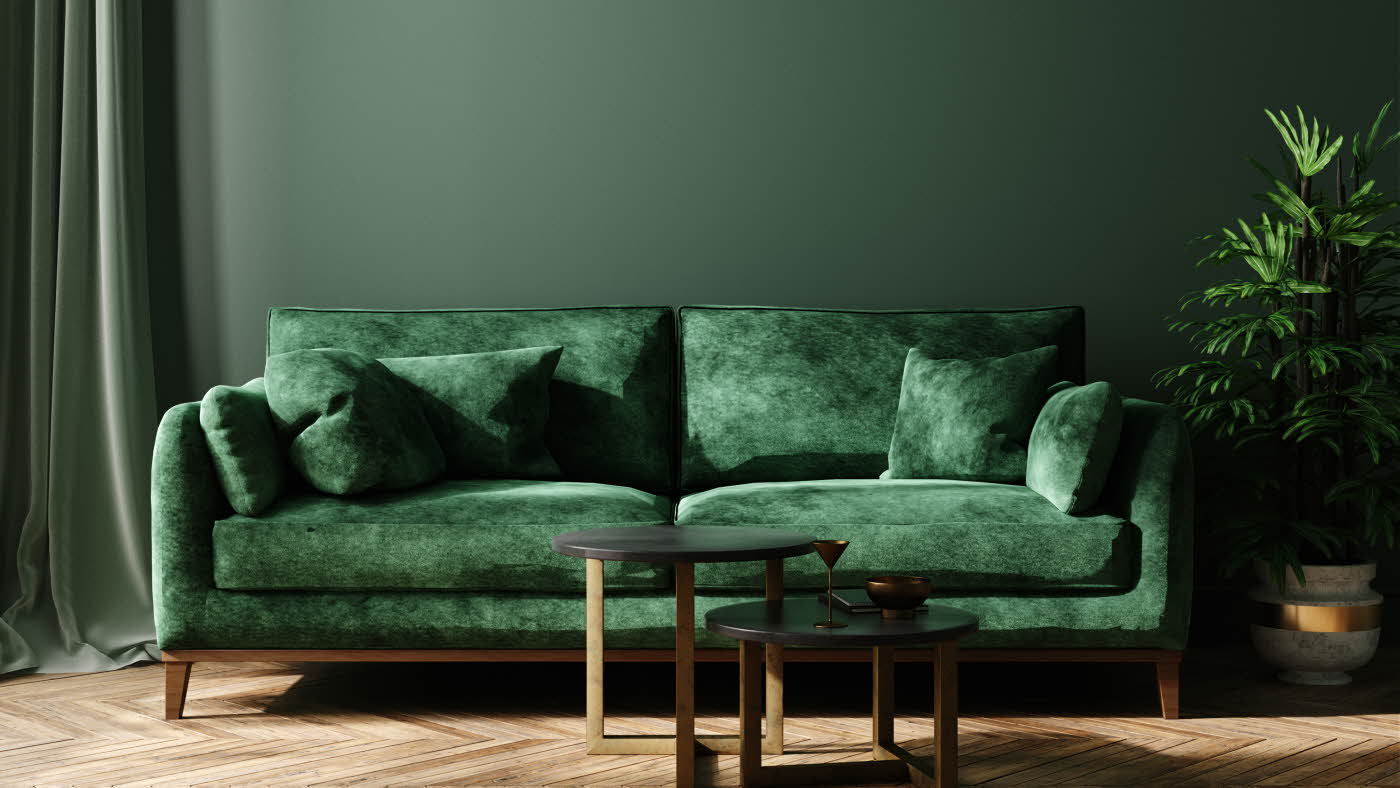 Mørkegrønn vegg med en matchende mørkegrønn sofa i fløyel, samt to små bord
