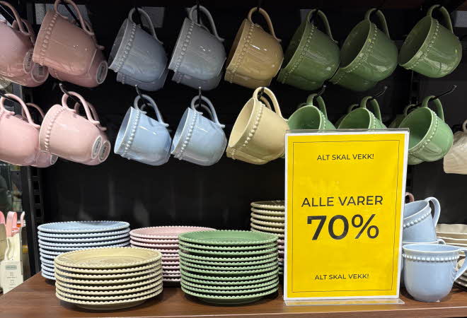 Kopper og skåler i rosa, blå og gule farger, står på en brun benk med sort bakgrunn