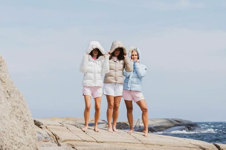 Tre kvinner i boblejakker og shorts går langs vannet