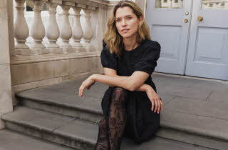 Dame sitter på steintrapp iført svart kjole med struktur og mønstrede strømpebukser.