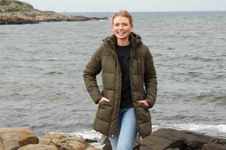 smilende dame ved vannet i grønn lang høstjakke