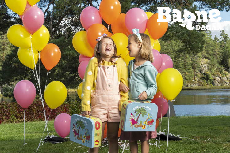 to born smiler og ler foran fargerike ballongar mens dei holder amfelia- og oskar-koffertar