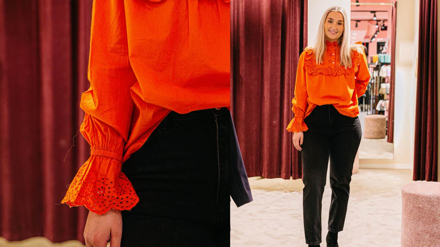 Dame med oransje bluse og mørke jeans