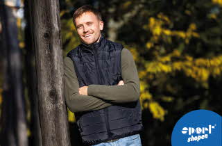 Mann med mørk vest og grønnskjorte lener seg mot et tre