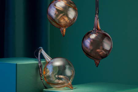 Tre Champagneklang julekuler fra Hadeland Glassverk, to som henger og en som ligger støttet opp.