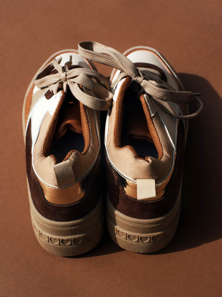 Nærbilde av sneakers med brune detaljer på brun bakgrunn sett bakfra