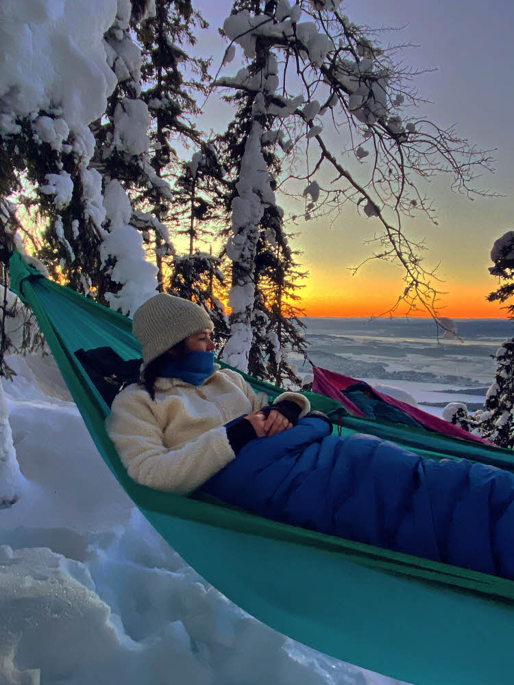 Pia Husøy som sover i hengekøye på vinteren med solnedgang i bakgrunn