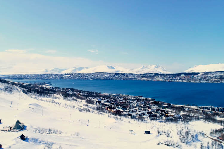 Vinterlandskap av en liten by med blå himmel og sol.
