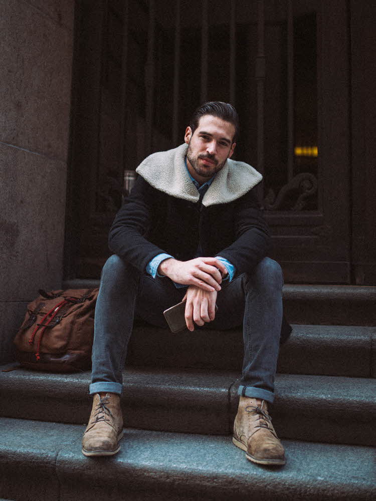 Mann med jakke med foret krage sitter på trapp utendørs og poserer for kamera