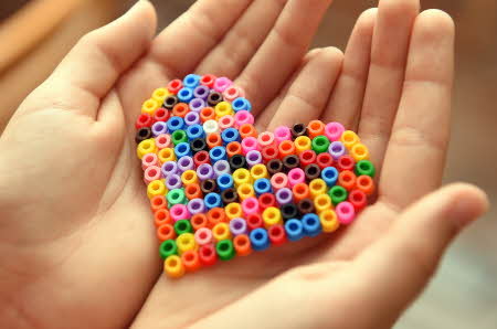 to hender som holder et hjerte laget av fargerike HAMA perler