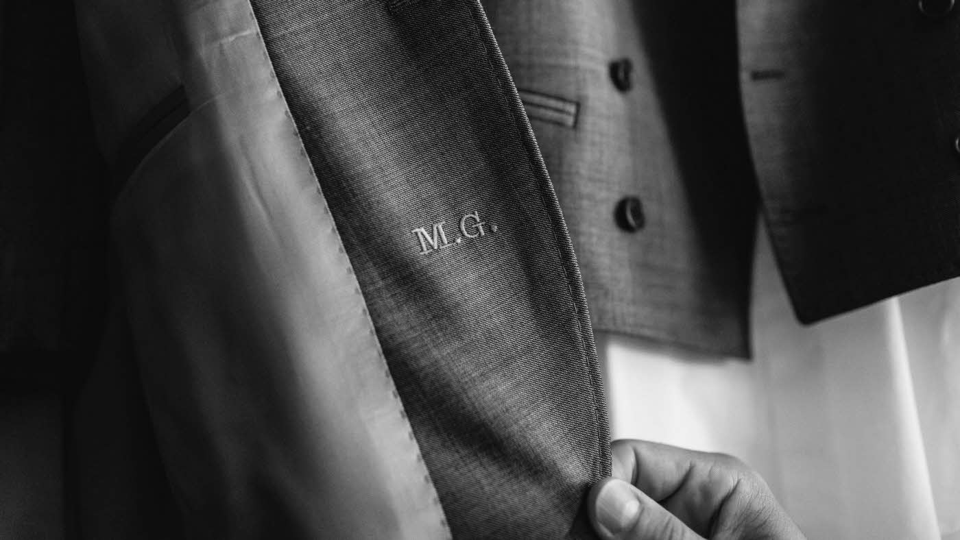 Hånd tar på en dressjakke, som er gravert med initialene M.G.