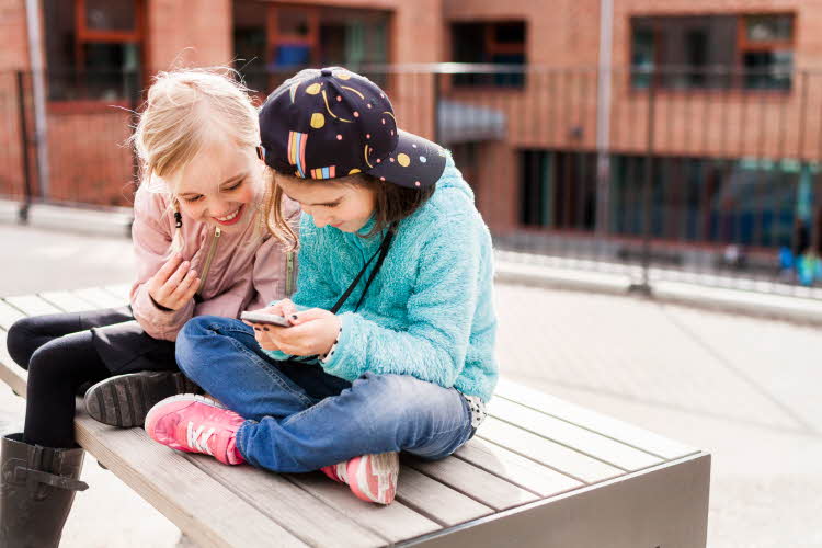 To jenter som sitter i skolegården mens de ser på en mobil